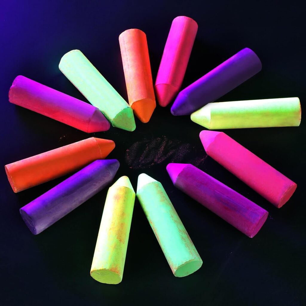 Twelve vibrant neon chalk sticks arranged in a circle on a black surface, with each stick pointing inward, creating a colorful and visually striking pattern.