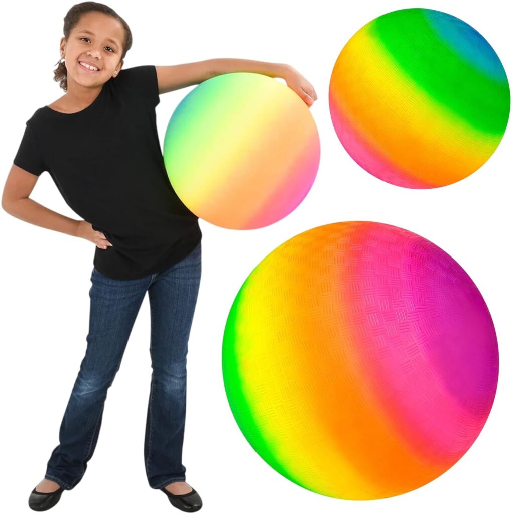 A smiling child in a black shirt and jeans stands next to three large, colorful rainbow gradient playground balls, one held under her arm and two shown separately on a white background.
